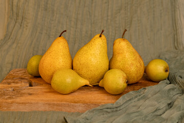Studio still life of ripe yellow pears arranged on a rustic wooden board with softly draped green fabric in the background.