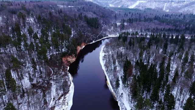 Snow-covered Gauja Valley near Sigulda, drone passes Devil&rsquo;s Cave, vivid cliffs