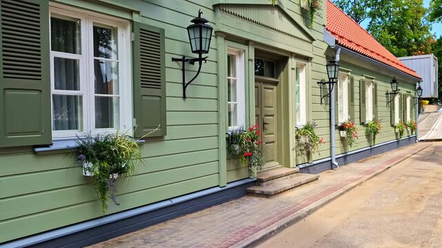 Classic green wooden villa with white windows, flower boxes and traditional shutters glows under summer sun in peaceful Jūrmala street.