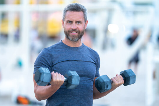 Sporty man lifting dumbbells outdoors. Sport man exercising with dumbbells in public outdoor gym. Fit guy working out in the park. Sportsman lifting dumbbells. Hispanic man training with dumbbells. - Powered by Adobe