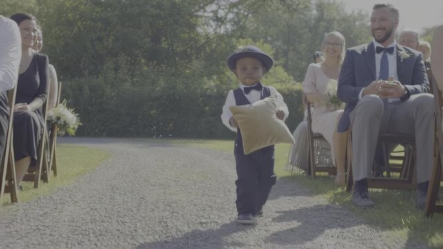 Young boy in suit carries pillow at outdoor ceremony