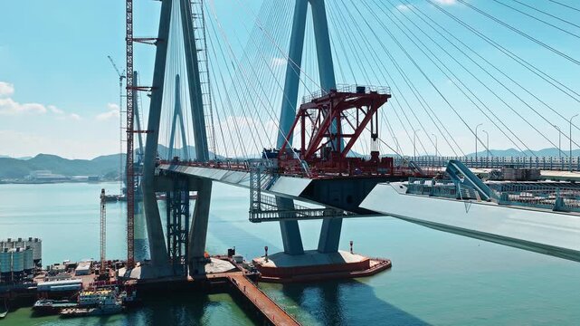Aerial shot of large cable stayed bridge under construction with heavy machinery over blue sea water