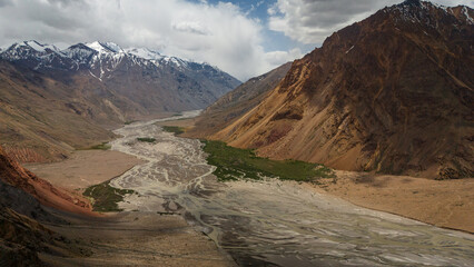 Aerial view over Bartang Valley in Tajikistan, showcasing rugged Pamir‑mountains terrain, a winding river, steep valleys and remote mountain villages