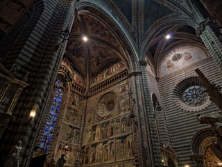 View of the interior of Orvieto Cathedral, a striking Gothic landmark, known for its striped marble, ornate facade, and rich frescoes. A masterpiece of Italian medieval art