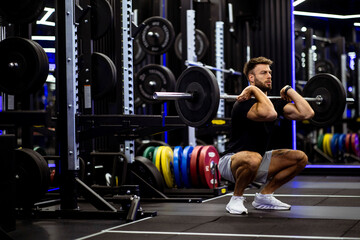 Man performing a barbell squat in a modern gym during morning workout session
