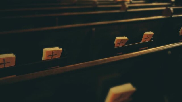 Smooth camera shot of wooden church pews and bibles with crosses. Catholic or Christian religious books and seating.
