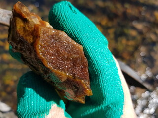 Bright orange druzy quartz specimen found in a sunny April stream, held by a turquoise glove, reflecting water bokeh