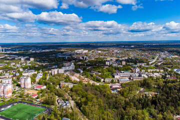 Aerial view of a sprawling city nestled among lush green spring foliage under a bright blue sky dotted with fluffy white clouds