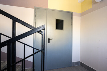 Secure metal door, staircase with black railing, interior walls in neutral colors, creating a functional and minimalist design for a commercial or institutional space