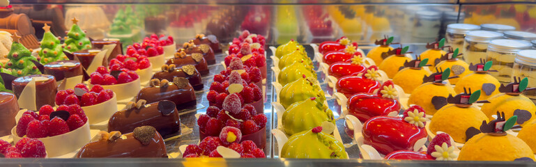 Delicious mix of different mini cakes displayed in a pastry shop. Colored desserts