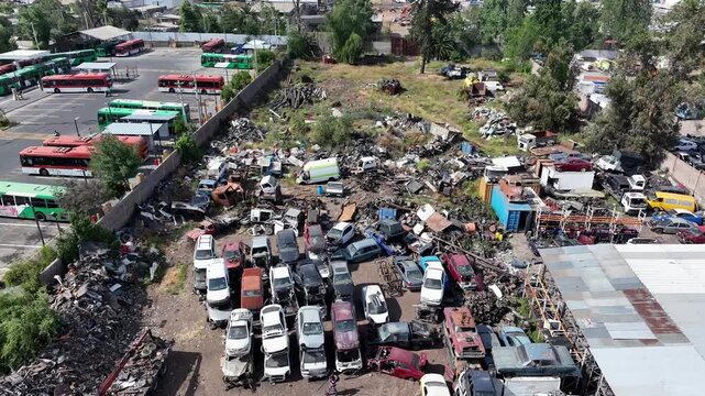 Forward drone aerial of junkyard with organized rows of scrapped cars, buses, warehouse buildings, and auto salvage depot overview