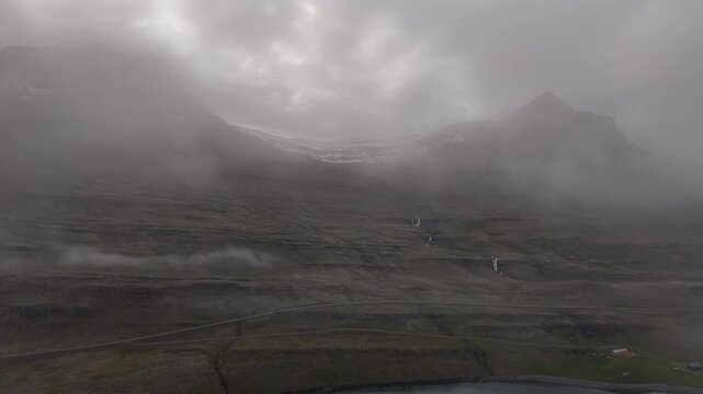 Misty mountain slopes and small waterfalls overlook Berufj&ouml;r&eth;ur as drifting clouds slide across the rugged Icelandic landscape
