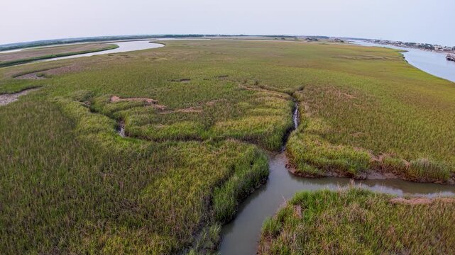 Drone footage captures green marshlands with winding waterways and tidal creeks near Charleston, South Carolina. The aerial view shows salt marsh vegetation and natural patterns under a pastel sky.
