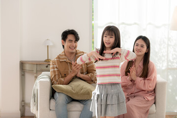 A young girl performs a dance for her parents in the living room while they smile and applaud