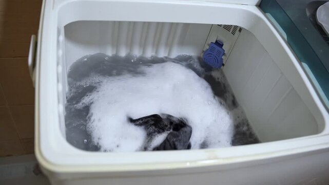 High-angle view of a top-loading washing machine during a high-speed spin cycle. Clothes and soapy water swirling rapidly inside the white plastic drum with visible motion blur.