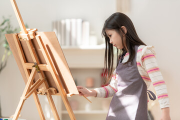 A little girl painting on an easel with focus and creativity in a living room at home