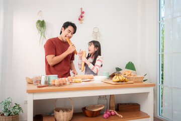 A father and daughter happily bite into baguettes in the kitchen