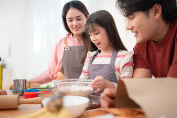 A family helping their daughter roll dough together in the kitchen, enjoying a fun baking moment