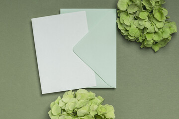 A card or invitation with two branches of hydrangea in green tones on an olive background. Blank letterhead and envelope with copy space.