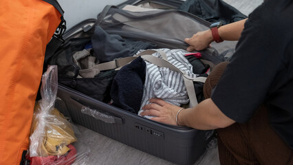 Asian woman packing clothes into an open suitcase, preparing for travel in a bright home setting