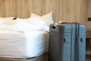 Big travel suitcase standing near the bed in a tidy room, suggesting vacation arrival or departure