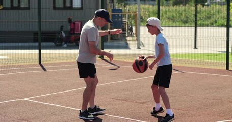Father and son play basketball on outdoor court in summer light. Dad coaches dribbling skills. Child practices movement. Scene shows active family sport and training. Basketball energy feels positive. - Powered by Adobe