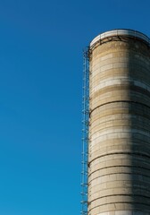 A massive cylindrical agricultural grain silo standing tall against a perfect, clear, deep blue summer sky on a sunny afternoon in the countryside ,concrete ,sunny ,industrial