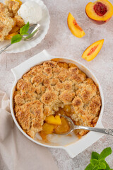 Homemade summer peach cobbler. Pie with juicy peaches, a scoop of vanilla ice cream and fresh mint on a white plate. Comfort food.