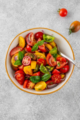 A salad of farm-fresh multi-colored tomatoes, red onions and fresh basil in a bowl on a gray concrete background. Healthy food. Top view.