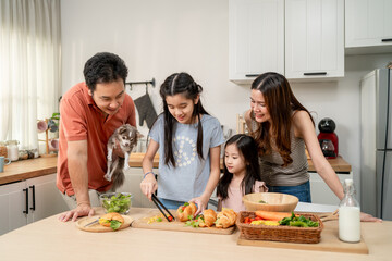 Asian parents bake bakery with their young daughters in kitchen at home.