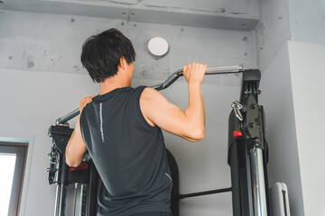 Young Asian man doing pull-ups on a chin-up machine at the gym
