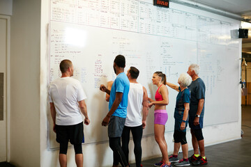 Writing, fitness and people by whiteboard in gym for workout planning with group class together. Health, training and back of athletes with exercise schedule for wellness routine in sports center.