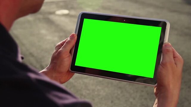 Person holding a tablet computer with a green screen, ready for chroma key compositing and digital content integration in outdoor setting