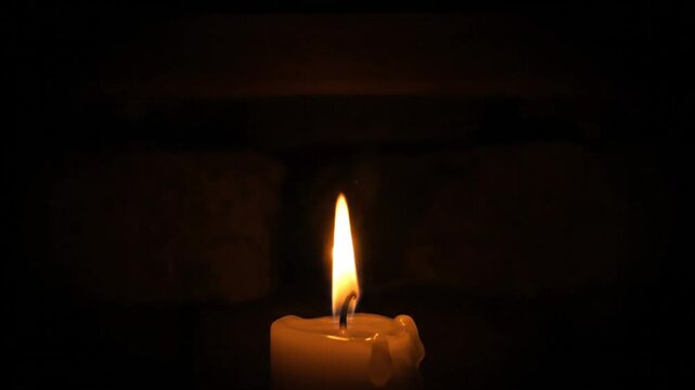 Bright candle flame burning brightly in a completely dark environment with soft background of a brick wall
