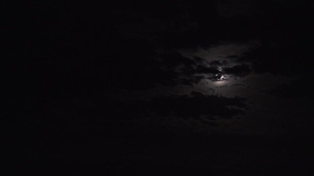Aerial footage capturing the ethereal beauty of a super moon obscured by dramatic night clouds. The moon's glow creates a mystical ambiance, enhanced by the expansive, silent sky.