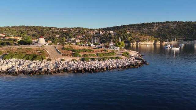 Kastos Island,aerial view forward and pan right overseeing the wind mill cafe and the harbor on a sunny day.Lot of boats at the town quay and outside on anchor.