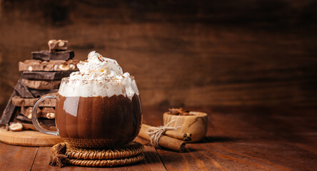 Hot chocolate with whipped cream, cinnamon and chocolate pieces on rustic wooden background with...
