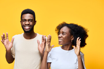 Happy young African American couple celebrating with joy against a bright yellow background, expressing excitement in casual attire with playful emotions