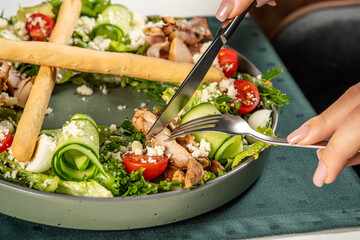 Hands cutting chicken in fresh salad bowl
