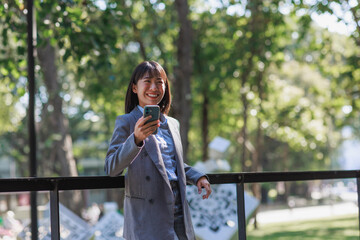 Young asian businesswoman smiling while using smartphone outdoors