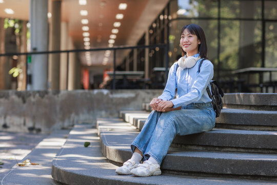 Happy young student woman sitting on campus stairs - Powered by Adobe
