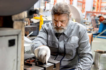 Senior male worker wearing safety clothing and gloves while working with machine at manufacturing factory. Elderly engineer technician operating machinery in industrial factory site.