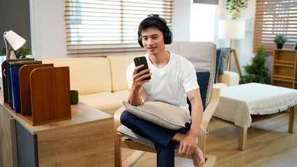 Smiling young man wearing headphones listen to mobile music playing in smartphone app, happy guy relaxing holding using phone enjoy favorite songs
