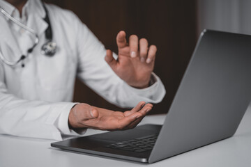 Doctor consulting online through laptop using hand gestures, symbolizing future teleconsultation and AI healthcare system concept on dark background.