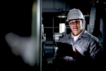 Young worker with tablet inspecting large metal tubes at factory during night shift. Engineer with...