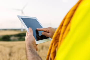 Engineer working at a wind farm, using a digital tablet to monitor renewable energy generation and environmental innovation. Renewable energy and industrial workforce concept