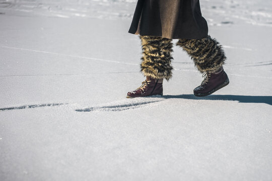 Young woman in warm stylish boots walking in winter nature. Close-up of warm winter boots and fur leggings walking on frozen snowy surface