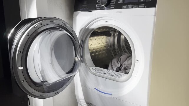 A woman opens the dryer door and loads a large red towel into the drum.