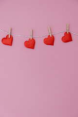 Red hearts hanging on a string against a pink background. The scene conveys a festive and romantic atmosphere, ideal for celebrations.