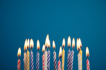 Lit multicolored birthday candles over blue background creating warm festive glow, with copy space for message or design. Perfect for birthday party invitations or greetings.